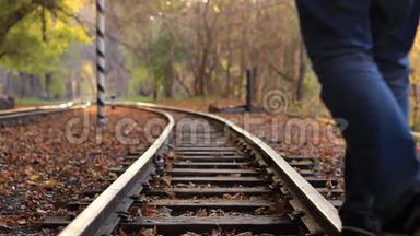 一个人走下火车轨道的背景金色秋天的森林。 一个人离开摄像机